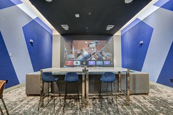 A room with a table with four chairs and a projection screen on the wall
